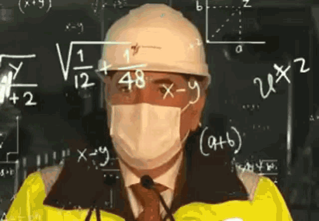a man wearing a hard hat and a mask is standing in front of a blackboard with mathematical equations .