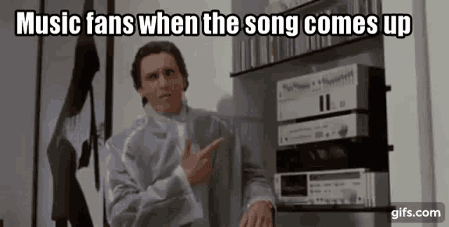 a man in a suit is pointing at a stack of stereos in a living room .