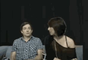 a man and a woman are sitting on a couch covering their faces with their hands .