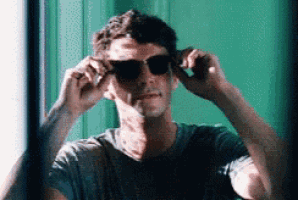 a man is adjusting his sunglasses in front of a mirror