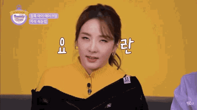 a woman wearing a yellow sweater and a black jacket is making a funny face in front of a sign that says another