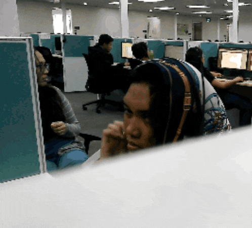 a woman in a head scarf sits in an office cubicle