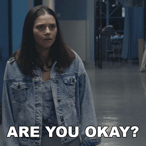 a woman in a denim jacket stands in a hallway and says " are you okay "