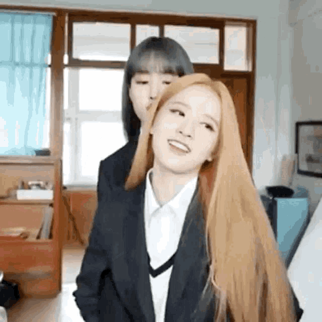 two girls are standing next to each other in a room . one of the girls has long blonde hair .