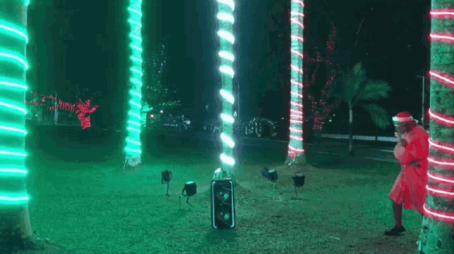 a man in a santa suit is standing in a park with christmas lights on the trees