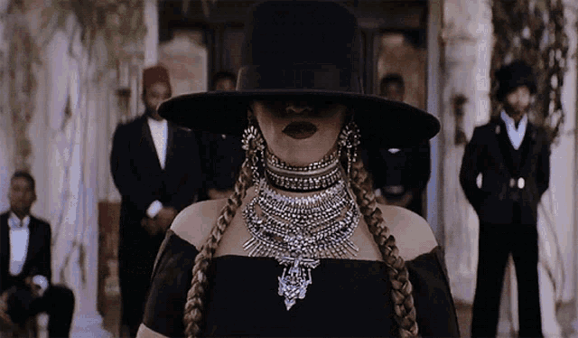 a woman in a black hat and necklace stands in front of a group of men in suits