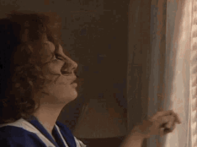 a woman is looking out of a window with blinds open