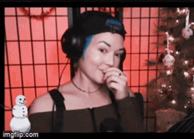 a woman wearing headphones and a hat is standing in front of a christmas tree and a snowman