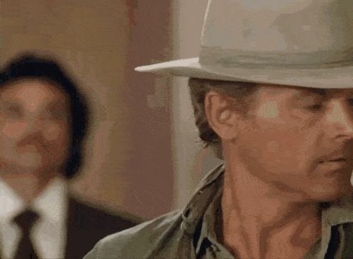 a man wearing a cowboy hat is standing in front of another man in a suit .