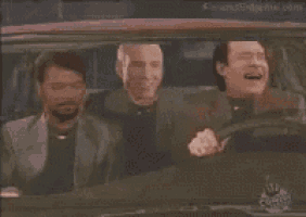 three men are sitting in a car laughing and looking out the window .