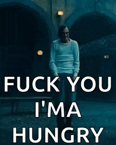 a man with a mustache is standing in front of a building and a sign that says fuck you i 'm hungry