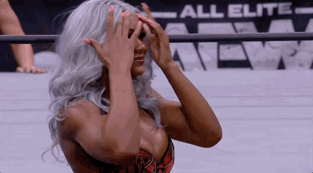 a female wrestler is covering her face with her hands while standing in a ring .