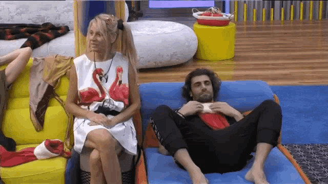 a woman in a flamingo shirt sits next to a man laying on a couch .