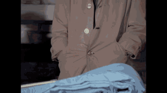 a man in a trench coat is standing next to a stack of clothes