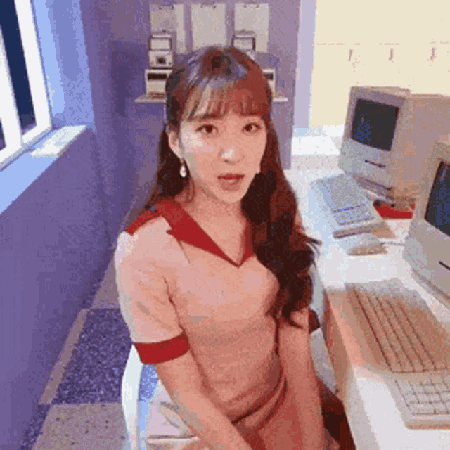 a woman is sitting at a desk with a computer in the background