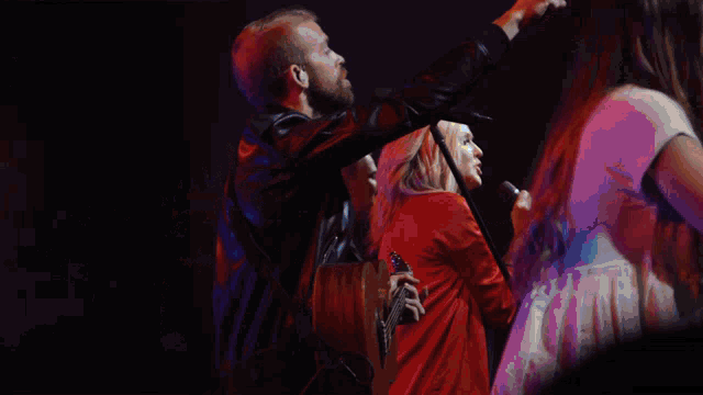 a man in a leather jacket stands in front of a microphone while a woman sings into it