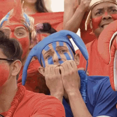 a man with blue paint on his face is sitting in a crowd of people