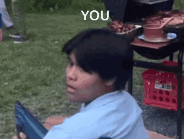 a young boy is sitting in the grass with the word you above his head .