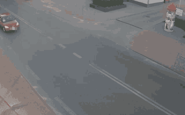 a red car is driving down a street while a man rides a motorcycle