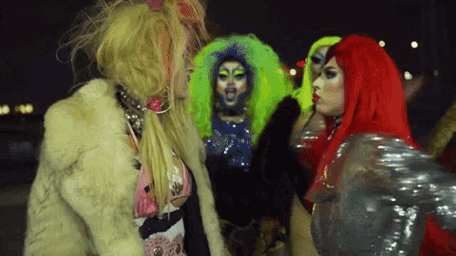 a group of drag queens are standing next to each other with one wearing a fur coat