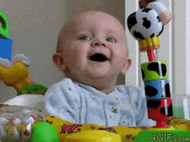 a baby is smiling while sitting in a crib next to a cow toy