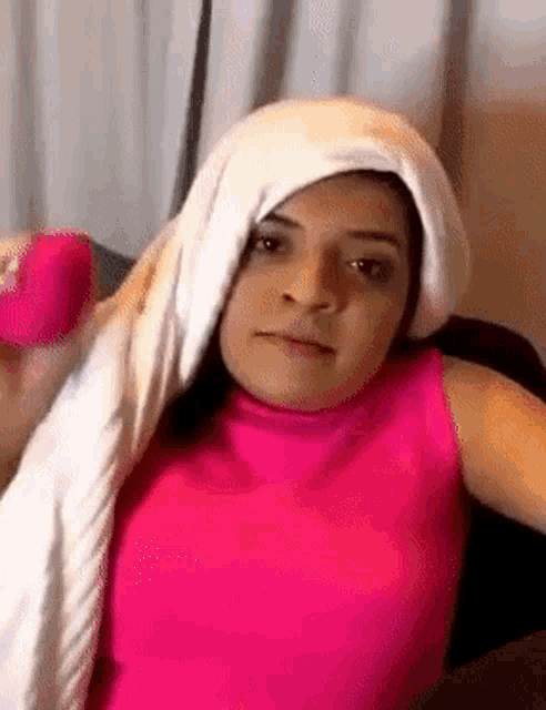 a woman in a pink tank top with a white towel wrapped around her head is holding a pink object