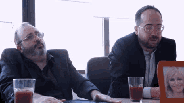 two men are sitting at a table with glasses of juice
