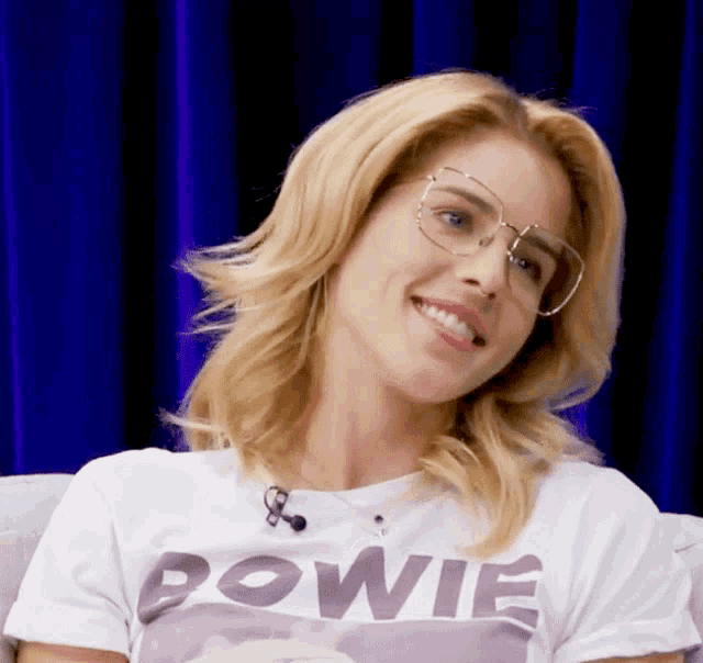 a woman wearing glasses and a bowie shirt smiles