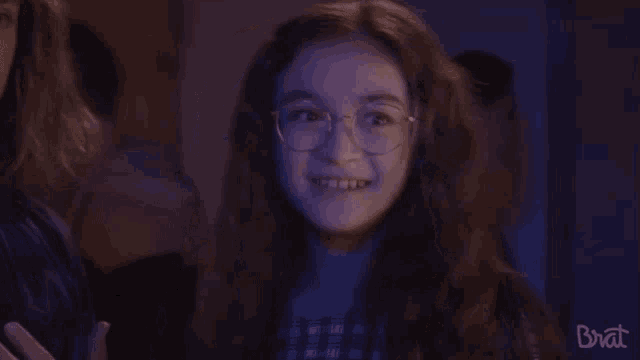 a girl wearing glasses and a plaid shirt is making a surprised face in a dark room .