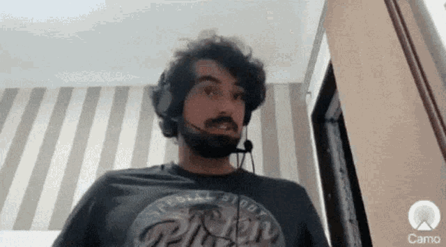 a man with a beard is wearing headphones and a camo logo in the corner