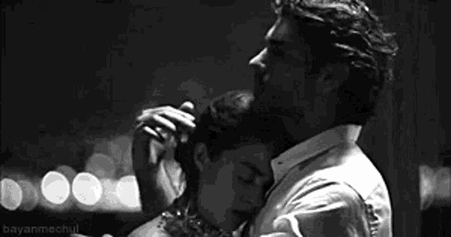 a black and white photo of a man kissing a woman on the cheek .