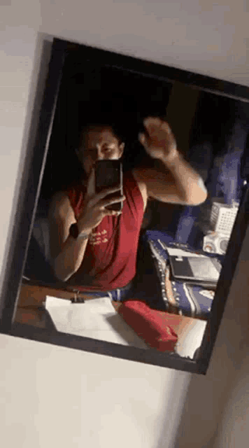 a man is taking a selfie in a mirror while wearing a red tank top .