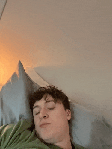 a young man is sleeping in a bed with his eyes closed