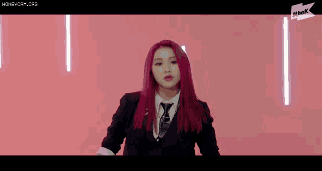 a woman with purple hair is wearing a suit and tie and making a funny face .