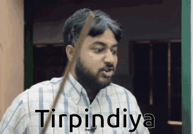 a man in a plaid shirt is holding a stick in his mouth and the word tinpinda is on the bottom
