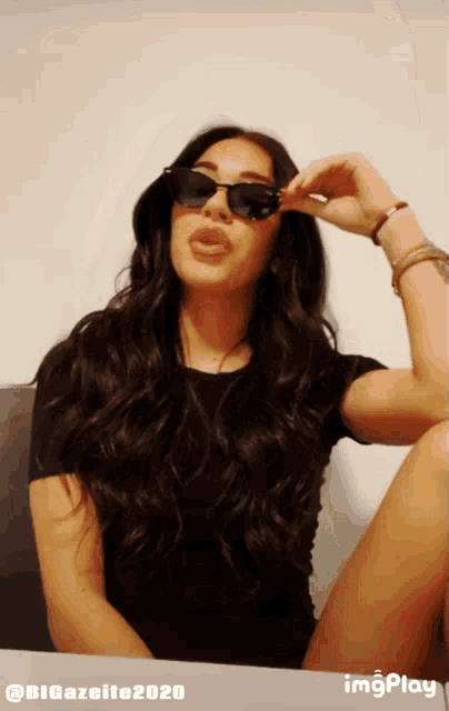 a woman wearing sunglasses is sitting at a table with imgplay written on the bottom right