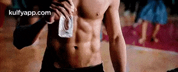 a man without a shirt is holding a bottle of water in his hand .
