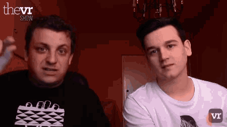 two men are standing next to each other in front of a red wall with the words thevi show on the bottom right
