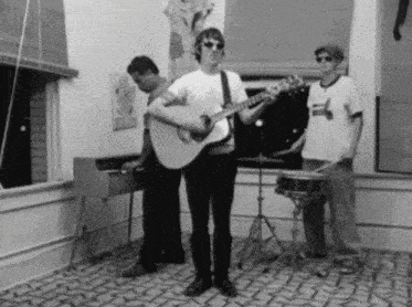 a man playing a guitar in a room with two other men playing instruments