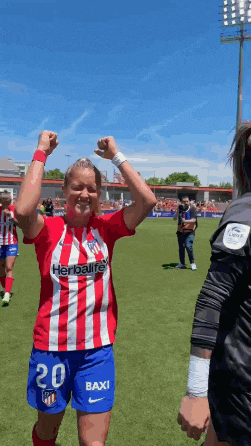 a female soccer player wearing a red and white striped shirt that says herbalife