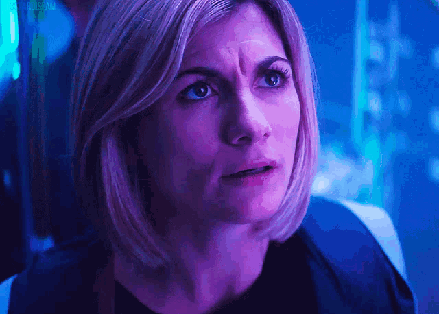 a close up of a woman 's face in a dark room with purple lights behind her