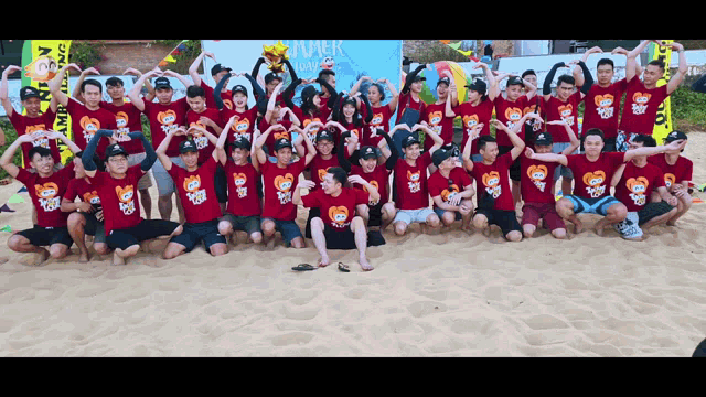 a group of people posing for a picture on a beach wearing red shirts that say summer camp