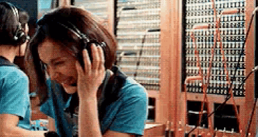 a woman wearing headphones is talking on a phone in front of a telephone switchboard .