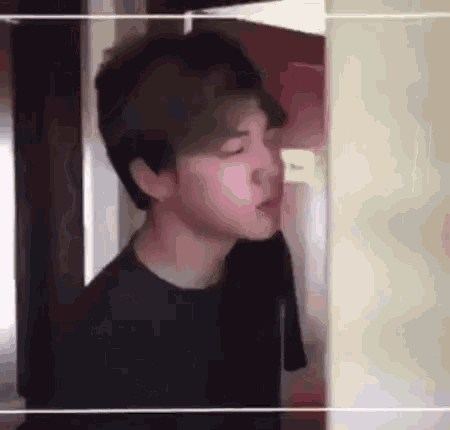 a young man in a black shirt is standing next to a wall in a room .