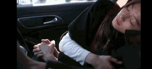 a woman is sleeping in a car while a man holds her hand