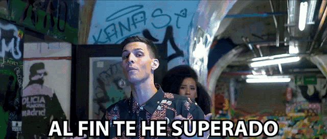 a man is standing in front of a wall that has graffiti on it and the words al fin te he superado