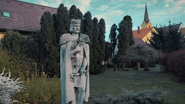 a statue of a man with a crown on his head is in a park