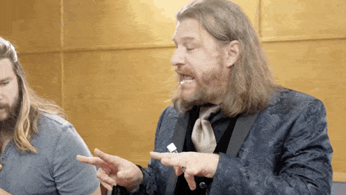 a man with long hair and a beard is pointing