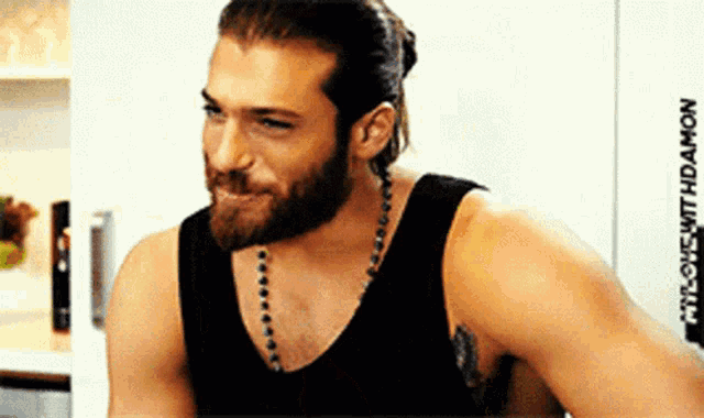 a man with a beard wearing a black tank top and a necklace is smiling .