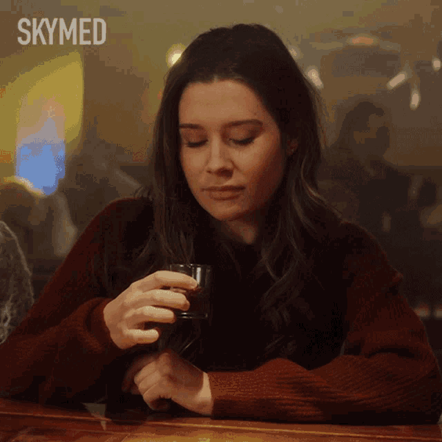 a woman sitting at a bar holding a glass with skymed written in the corner